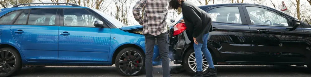 Young Male And Female Drivers Inspecting Damage After Road Traffic Accident